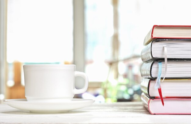 Photo tasse de café classique blanche sur une table blanche sur la terrasse et une pile de livres avec des signets lisant l'apprentissage et étudiant les heures du matin pour l'auto-éducation