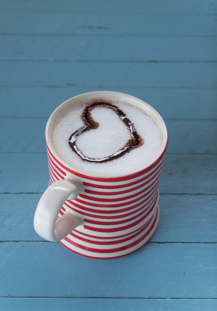 Tasse à café avec coeur latte art sur planche de bois bleue