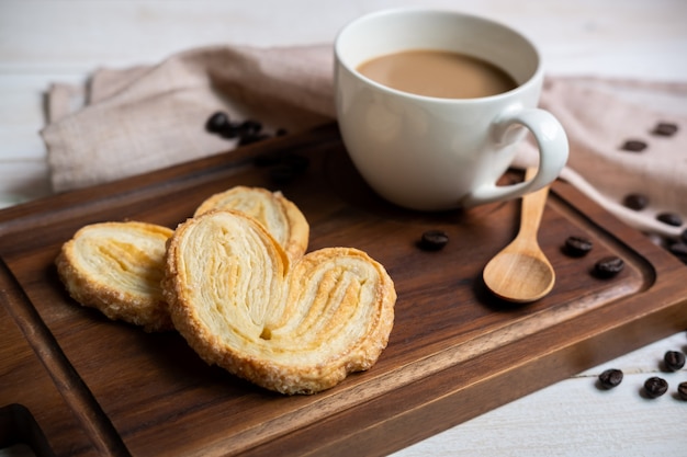 Tasse de café avec des collations sur une planche à découper en bois sur une table en bois blanche