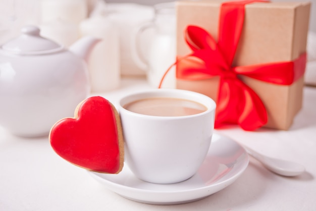 Tasse de café et un cookie rouge en forme de coeur avec boîte-cadeau et théière sur le tableau blanc