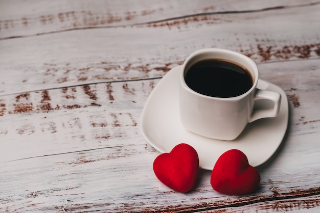 Tasse De Café Et Un Couple De Coeurs Rouges De Saint Valentin Sur Une Table En Bois Blanche. Le Concept De Carte De Voeux