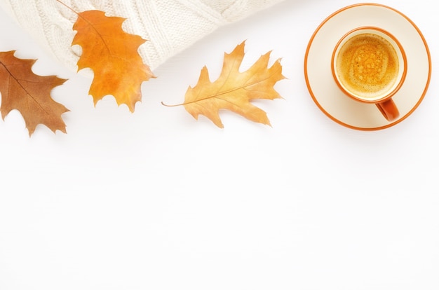 Une tasse de café, une couverture tricotée et des feuilles d'automne sur un fond en bois blanc