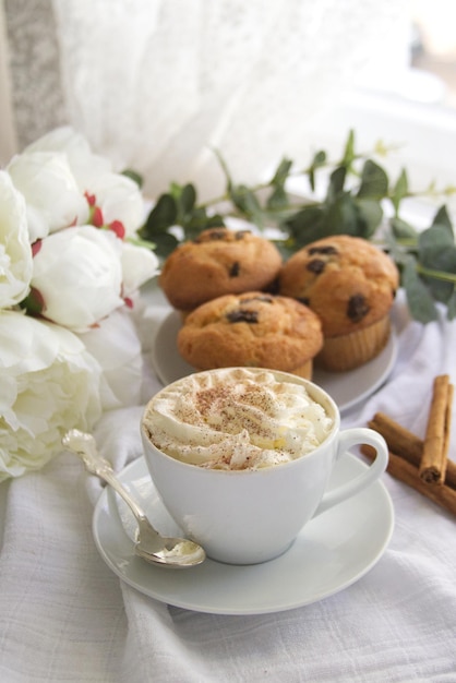 Une tasse de café avec de la crème fouettée à côté d'une assiette sur laquelle se trouvent des muffins au chocolat