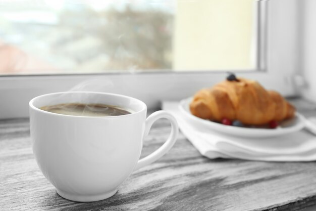 Tasse de café et croissant sur le rebord de la fenêtre