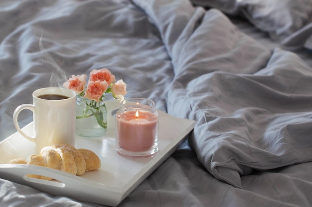 Tasse de café avec croissant et roses roses sur le lit dans la chambre