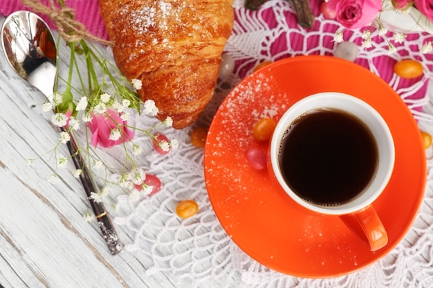 Tasse de café et croissant sont décorés par la petite Tour Eiffel, serviettes, roses et bonbons sur une table en bois blanc