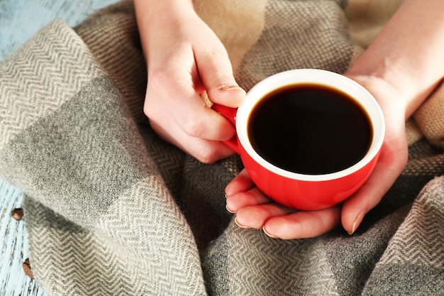 Tasse de café dans les mains sur fond plaid