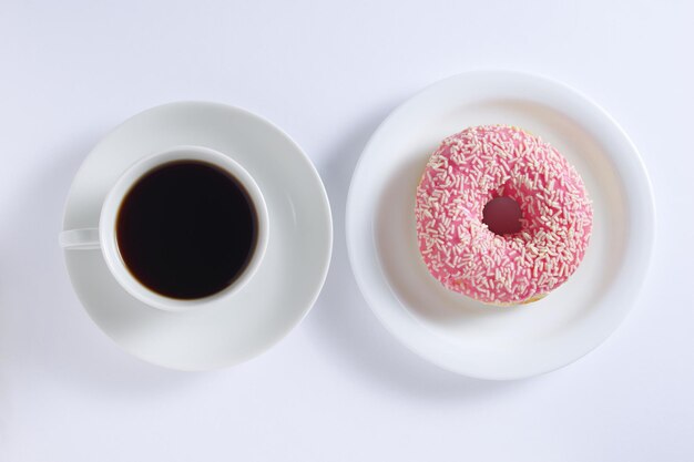 Une tasse de café et un donut rose sur une assiette sur fond blanc