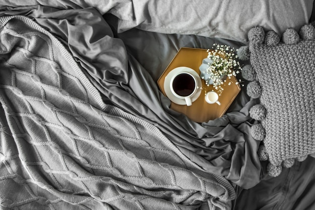 Tasse à café avec du lait et des fleurs sur un plateau au lit