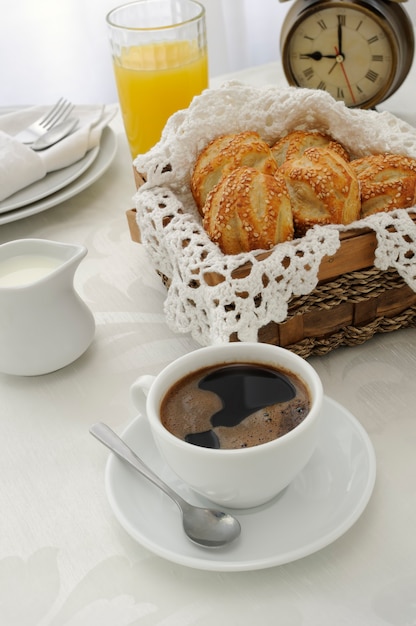 Tasse de café du matin avec des petits pains fraîchement préparés avec des graines de sésame, du jus et du lait