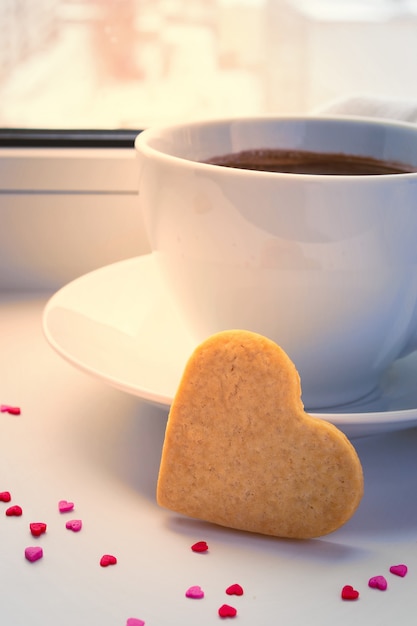 Tasse de café du matin sur un rebord de fenêtre d'hiver. Coeurs de cookie. Saint Valentin romantique
