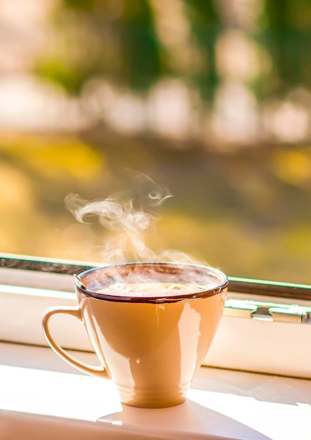 Tasse de café du matin sur un rebord de fenêtre Vapeur au-dessus de la tasse en céramique