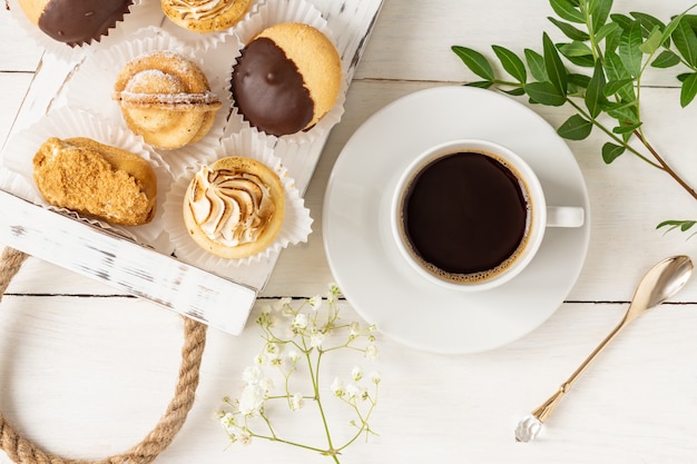 Tasse de café du matin avec de savoureux desserts fraîchement préparés décorés de feuilles et de fleurs.