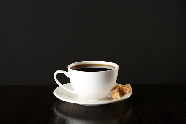 Tasse de café avec du sucre en morceaux sur une table en bois sur fond sombre