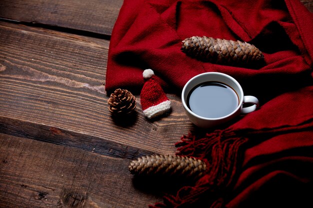 Tasse de café, écharpe rouge et chapeau de père Noël avec des pommes de pin sur table en bois