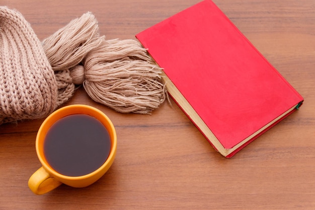 Tasse de café, écharpe tricotée et livre sur fond de bois