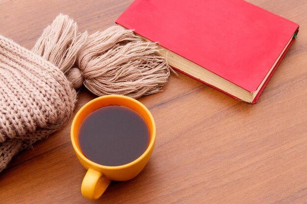 Tasse de café, écharpe tricotée et livre sur fond de bois