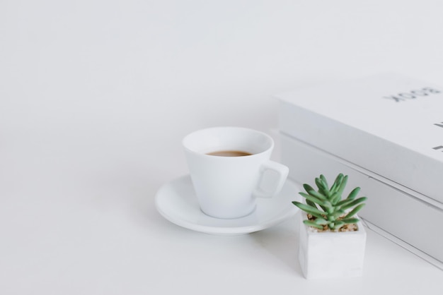 Une tasse de café empiler des livres et une plante décorative sur fond blanc Papier peint de bureau minimaliste