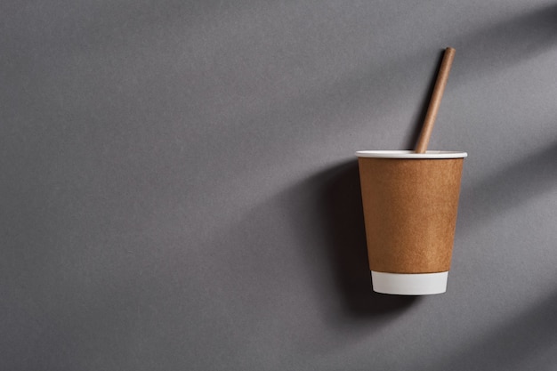 Tasse de café à emporter marron avec paille en papier avec des ombres profondes de la fenêtre sur fond de couleur gris tendance. Concept zéro déchet. Vue de dessus.