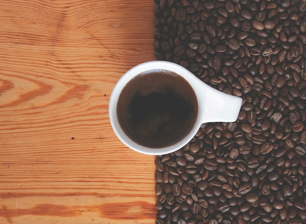 Une tasse de café entre une surface en bois et des grains de café torréfiés.