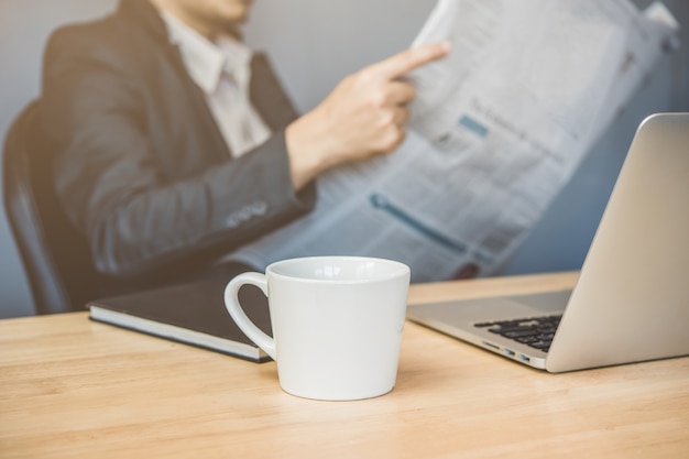 Tasse de café sur l&#39;espace de travail avec l&#39;homme d&#39;affaires en lisant le journal