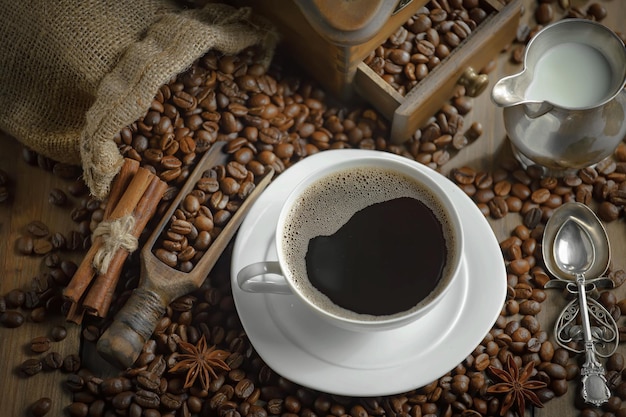 Une tasse de café est posée sur une table à côté de grains de café et de bâtons de cannelle.