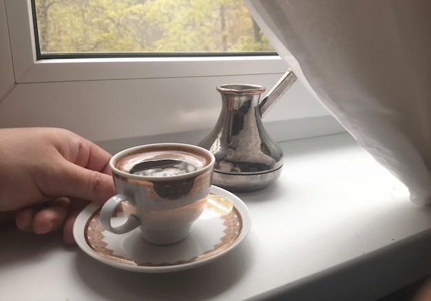 Une tasse de café expresso chaud et un cezve sur le rebord de la fenêtre le matin Toile de fond d'arôme d'arabica aux couleurs douces