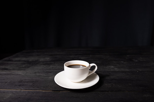 Tasse de café expresso sur table noire vintage, vue de face. Café dans une tasse blanche sur une surface sombre avec une agréable texture de bois ancien