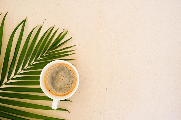 Tasse de café sur feuille de palmier sur fond de sable