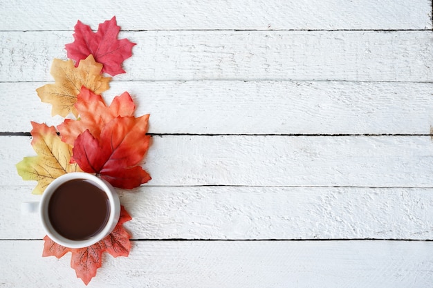 Tasse à café sur les feuilles d'automne et fond de surface en bois blanc, espace pour copie