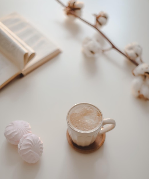 Tasse à café fleur de coton livre ouvert sur une vue de dessus de fond de table blanche