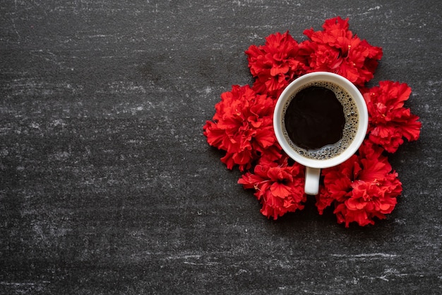 Tasse de café, fleur rouge sur table noire.