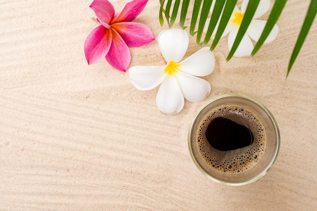 Une tasse de café avec des fleurs sur une plage