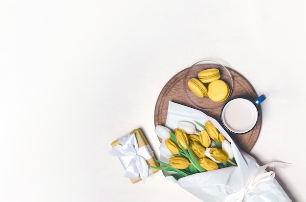 Tasse à café, fleurs de tulipes jaunes et macarons jaunes sur table en bois