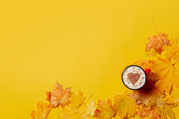 Tasse de café en forme de coeur et feuilles d'érable autour sur fond jaune.