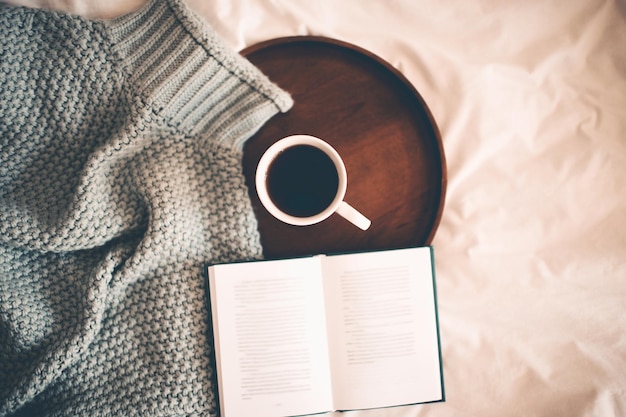 Tasse de café frais chaud avec livre ouvert et jersey tricoté au lit en gros plan. Bonjour. Vue de dessus.