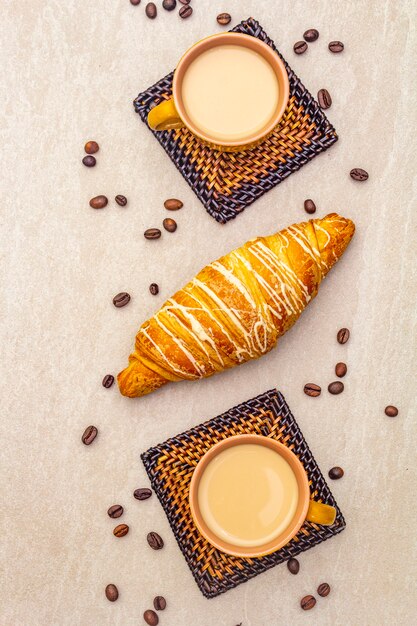 Une tasse de café frais avec un croissant. Le concept sur une surface en pierre avec des grains de café torréfiés et des sous-verres en osier, vue de dessus, gros plan.