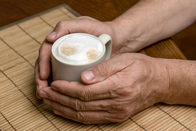 Une tasse de café frais avec de la mousse de cappuccino dans les mains d'un homme en gros plan