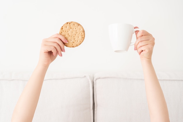 Tasse de café et gâteau en mains au-dessus d'une couverture au lit. Femme se réveillant le matin