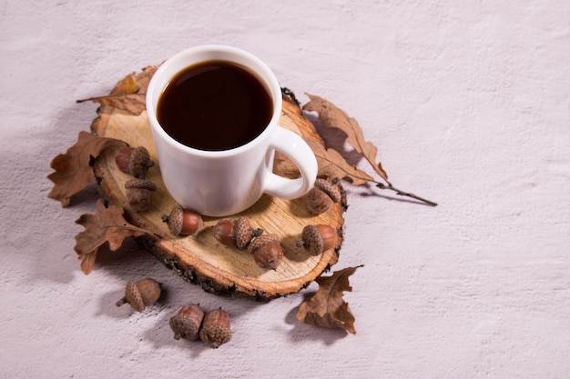 Tasse à café de gland blanc sur une section en bois avec des glands et des feuilles de chêne sur fond clair