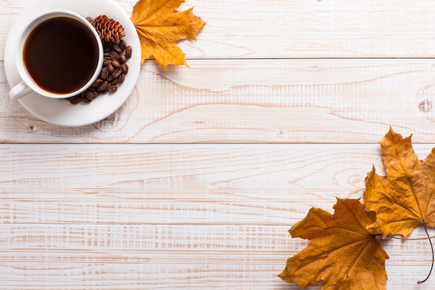 Tasse de café avec des grains de café épars, des feuilles jaunes sèches sur une table en bois. Humeur matin d'automne, fond.