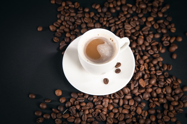 Tasse de café avec des grains de café sur le fond noir