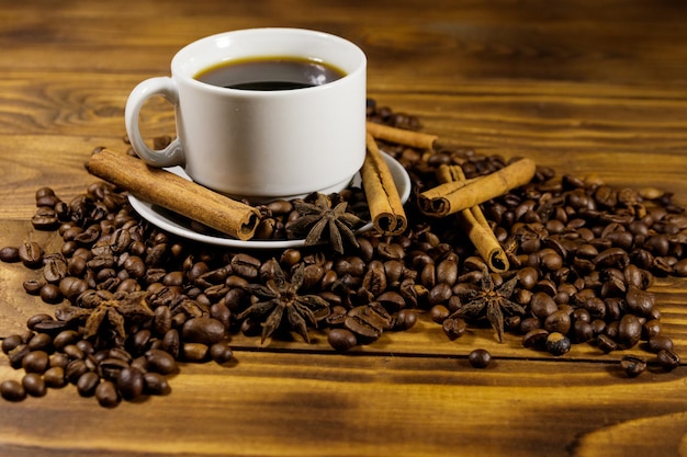 Tasse de café, grains de café torréfiés, anis étoilé et bâtons de cannelle sur table en bois