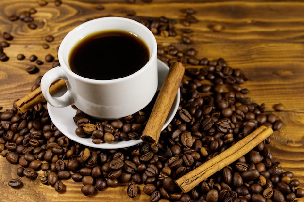 Tasse de café, grains de café torréfiés et bâtons de cannelle sur table en bois