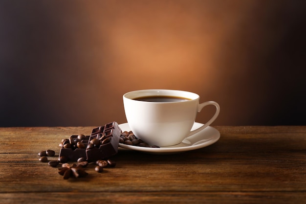 Tasse de café avec des grains et du chocolat sur une table en bois sur fond sombre