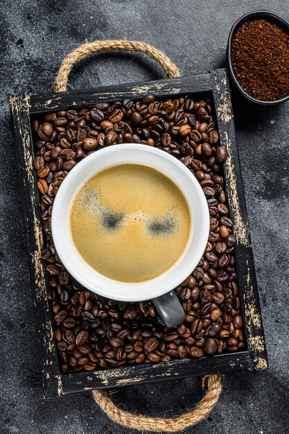 Tasse à café et haricots dans le vieux plateau en bois sur table noire. Vue de dessus.