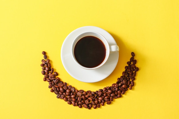 Tasse de café avec des haricots dispersés sur un fond jaune