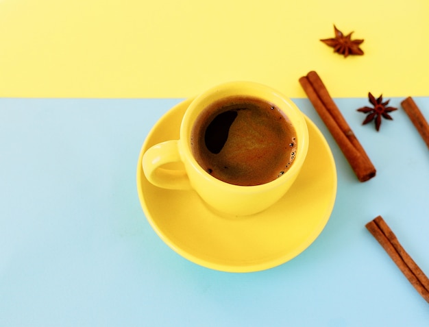 Tasse à café jaune sur un double fond jaune et bleu avec des bâtons d'anis et de cannelle