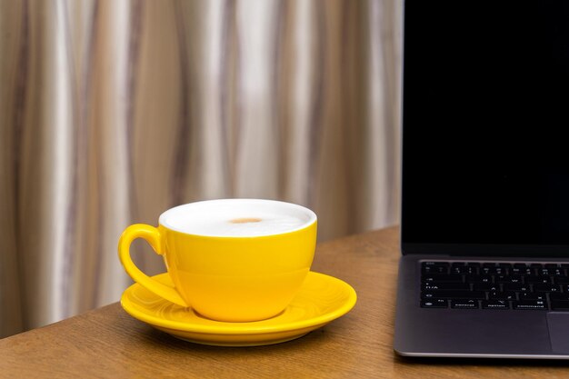 Tasse à café jaune et ordinateur portable sur table en bois