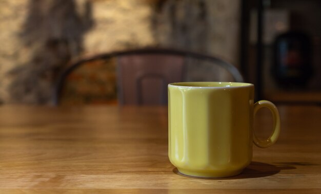 Une tasse de café jaune sur une table en bois.